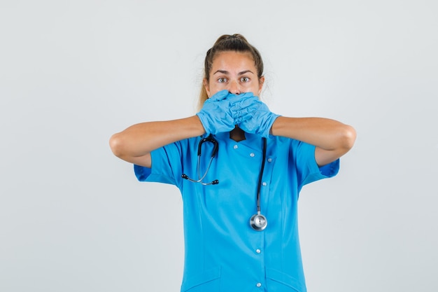 Female doctor covering mouth with hands in blue uniform