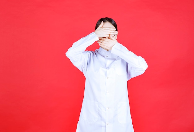 Free photo female doctor in eyeglasses standing on red background and feeling tired and sleepy.