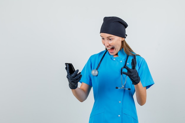 여성 의사 유니폼, 장갑에 스마트 폰을 보면서 행복을 찾고 몸짓. 전면보기.