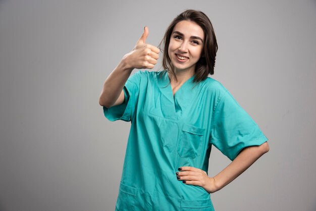 Female doctor giving thumbs up on gray background. High quality photo