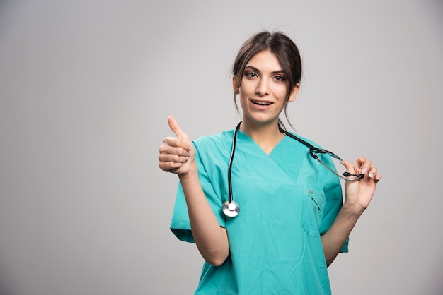 Female doctor giving thumbs up on gray