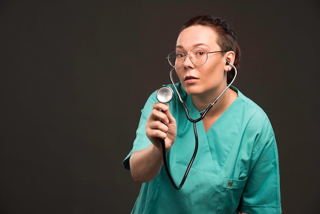 Foto gratuita dottoressa in uniforme verde che tiene uno stetoscopio e ascolta il paziente.