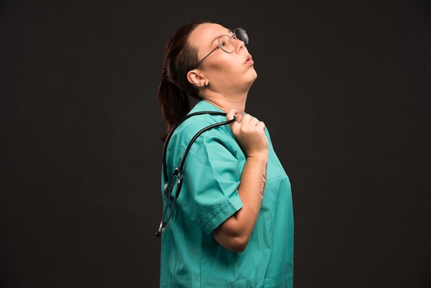 Female doctor in green uniform holding a stethoscope and looks bored. 