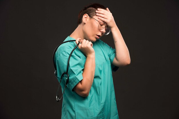 Female doctor in green uniform holding a stethoscope and looks tired.