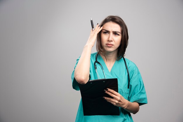 Medico donna che ha mal di testa su sfondo grigio. foto di alta qualità