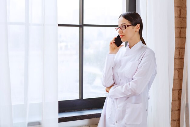 Female doctor having an important phone call near window .