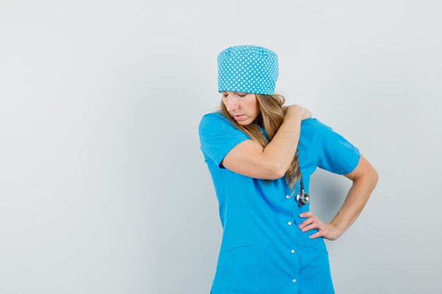 Female doctor having shoulder pain in blue uniform and looking uncomfortable 