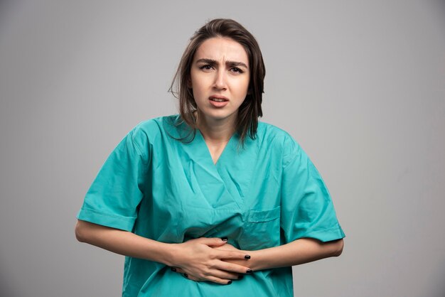 Female doctor having stomach ache on gray background. High quality photo