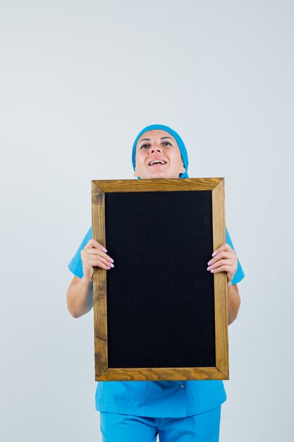 Female doctor holding blackboard in blue uniform and looking cheery. front view.
