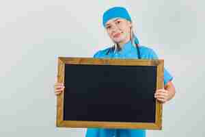 Free photo female doctor holding blackboard and smiling in blue uniform