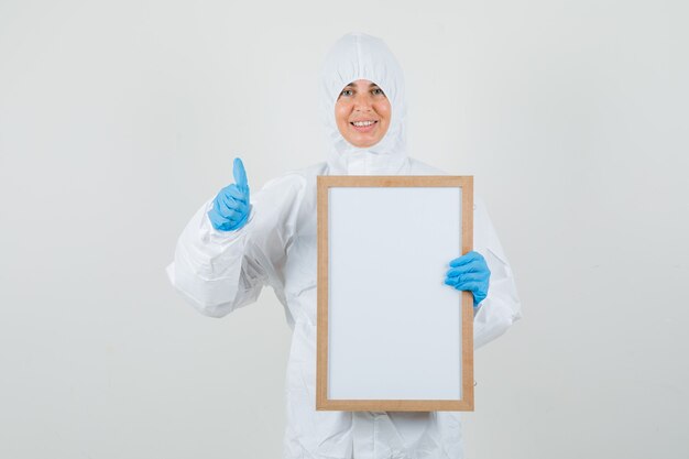 Женщина-врач держит пустую рамку с большим пальцем в защитном костюме
