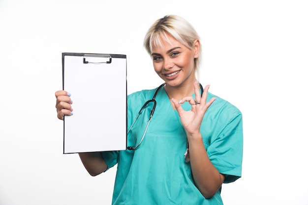 Female doctor holding a clipboard making ok gesture on white surface