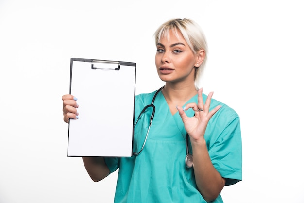 Female doctor holding a clipboard making ok gesture on white surface