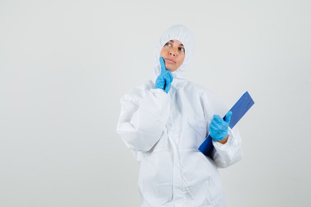 Free photo female doctor holding clipboard, pen while looking up in protection suit