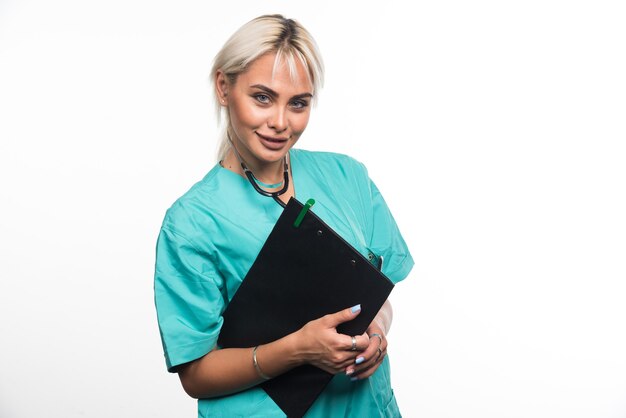 Female doctor holding clipboard on white wall .