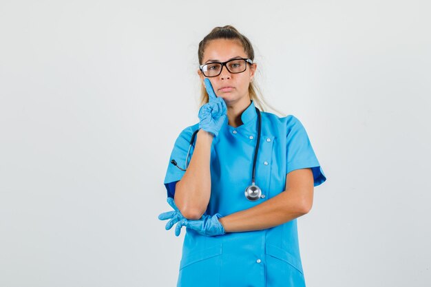 파란색 유니폼에 뺨에 손가락을 잡고 여성 의사