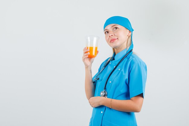 파란색 유니폼을 입고 쾌활한 찾고있는 동안 주스 잔을 들고 여성 의사