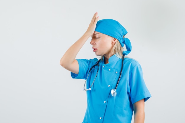 Female doctor holding hand on forehead in blue uniform and looking tired