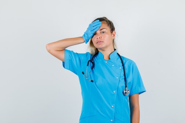 Female doctor holding hand on forehead in blue uniform