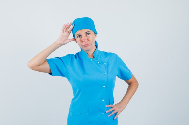 青い制服を着て頭を抱えて混乱している女性医師。正面図。