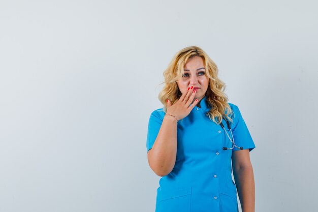 Female doctor holding hand on her lip in blue uniform and looking upset. space for text