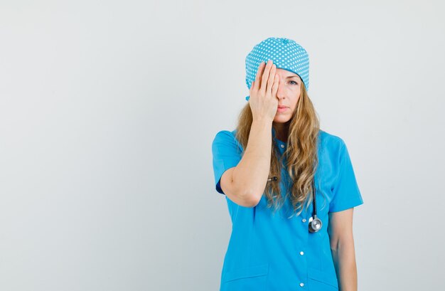 Female doctor holding hand on one eye in blue uniform 