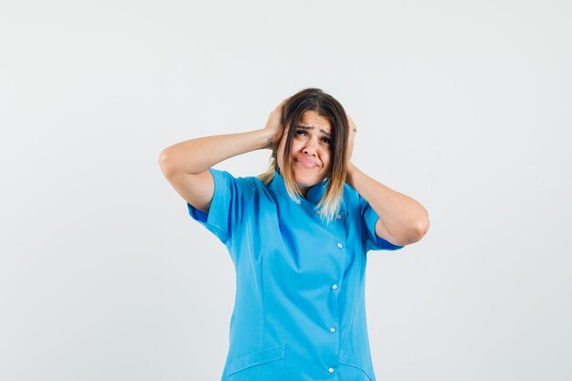 Female doctor holding hands on ears in blue uniform and looking annoyed