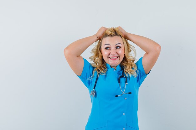Женщина-врач, держащая руки на голове в синей форме и веселый вид