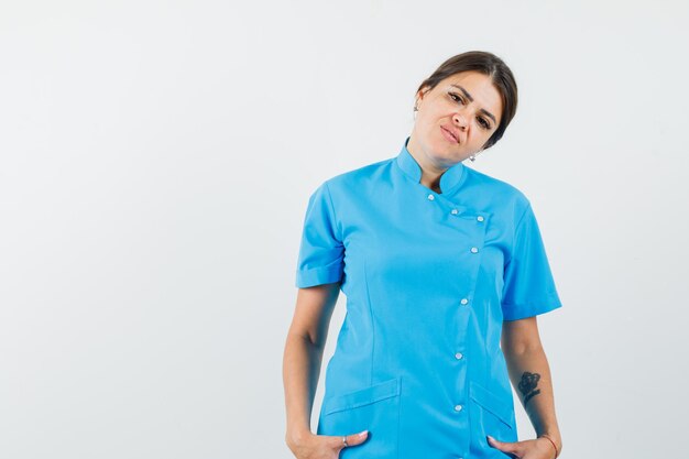 Женщина-врач держится за руки в карманах в синей форме и выглядит уверенно