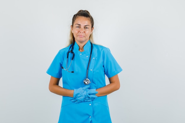 Female doctor holding hands on stomach in blue uniform, gloves and looking painful.