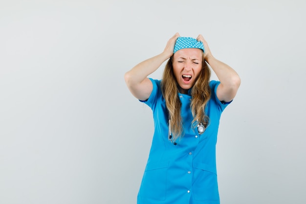 Female doctor holding head while screaming in blue uniform and looking mournful 