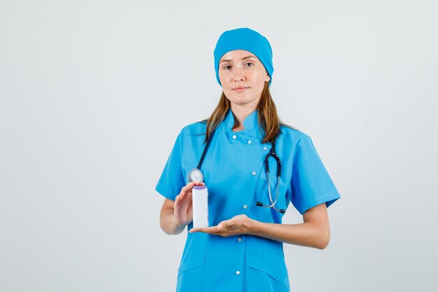 Female doctor holding medical bottle in blue uniform and looking careful