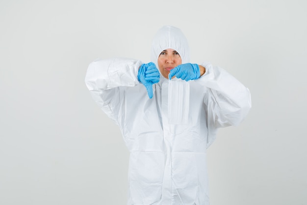 Female doctor holding medical mask with thumb down in protection suit