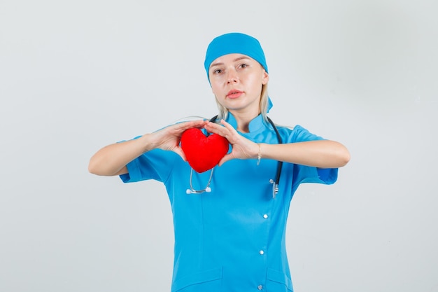 Free photo female doctor holding red heart in blue uniform and looking serious