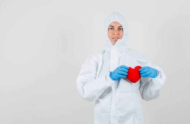 Женщина-врач держит красное сердце в защитном костюме