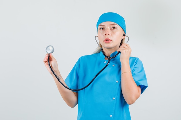 Female doctor holding stethoscope in blue uniform and looking serious