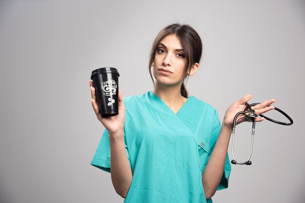 聴診器と一杯のコーヒーを保持している女性医師