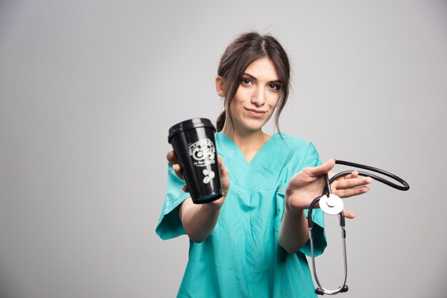 Female doctor holding stethoscope and cup of coffee