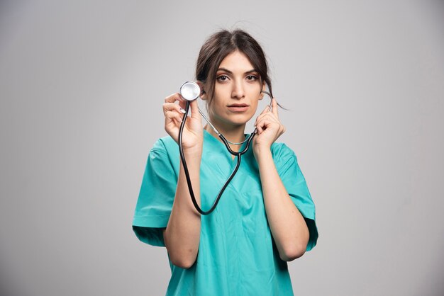 Женщина-врач, держащая стетоскоп на сером
