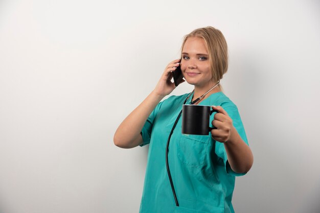 Female doctor holding tea while talking with telephone.