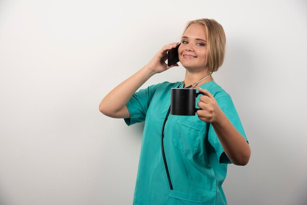 Female doctor holding tea while talking with telephone.