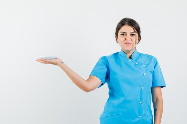 Female doctor holding white saucer in blue uniform and looking confident