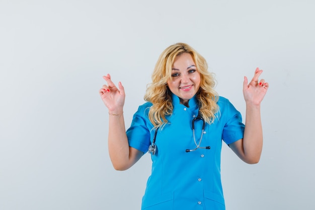 Бесплатное фото Женщина-врач в синей форме держит пальцы скрещенными и выглядит весело