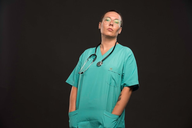 Женщина-врач в зеленой форме держит стетоскоп и выглядит уверенно.