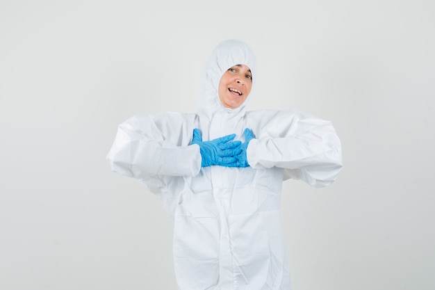Female doctor keeping hands on chest in protection suit, gloves and looking grateful