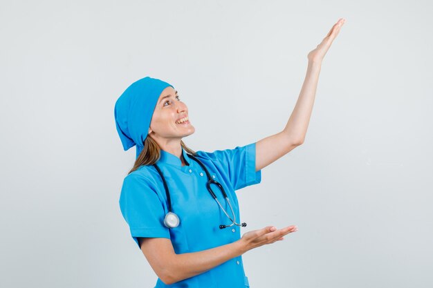 Female doctor keeping palms open to show something in uniform and looking glad. front view.