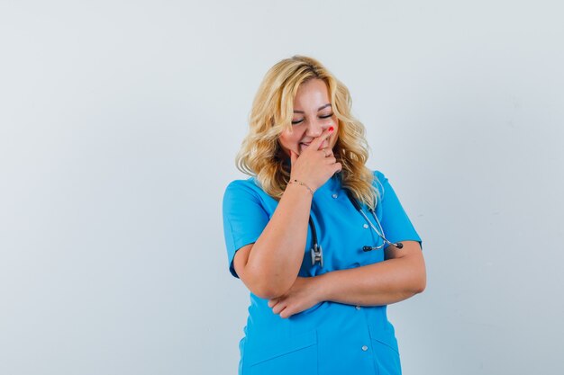 Free photo female doctor laughing with hand on mouth in blue uniform and looking glad space for text