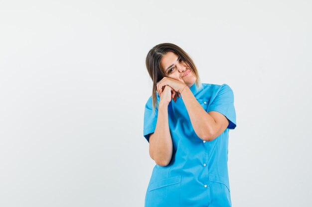 Female doctor leaning cheek on clasped hands in blue uniform and looking relaxed