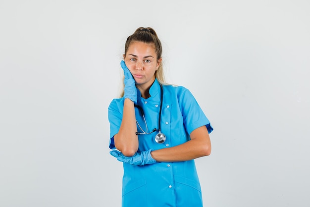 Female doctor leaning cheek on raised palm in blue uniform
