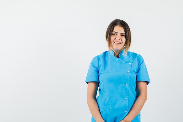 Женщина-врач смотрит в камеру и улыбается в синей форме